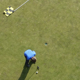 Man putting golf ball next to flag and hole