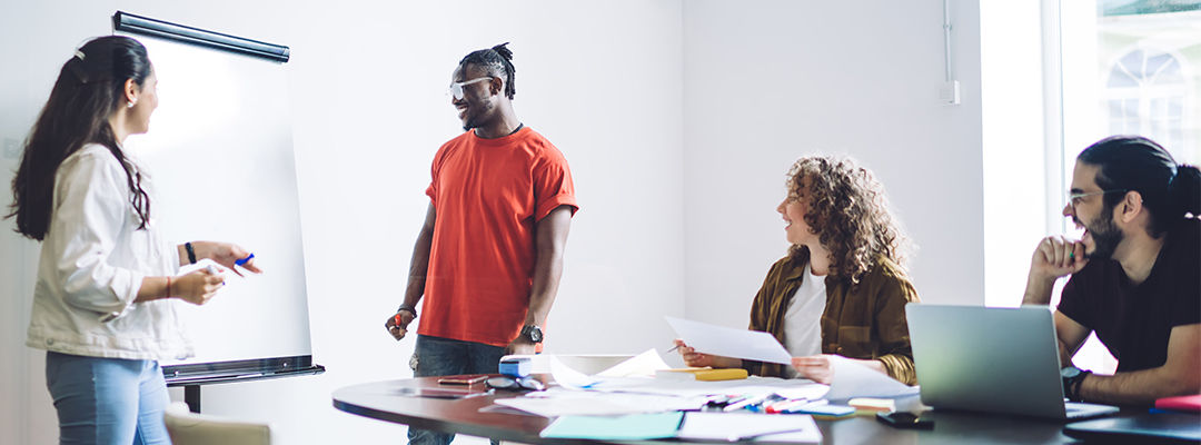 Multiracial happy professional employees looking at blank marker board during cooperation about company strategy and development around table in light boardroom