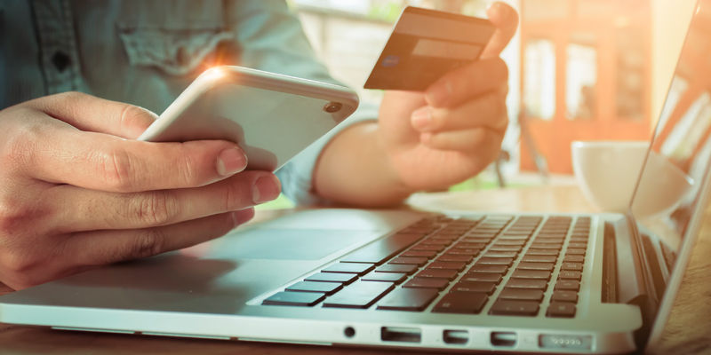 Person at a laptop purchasing an item online with phone and credit card in hand