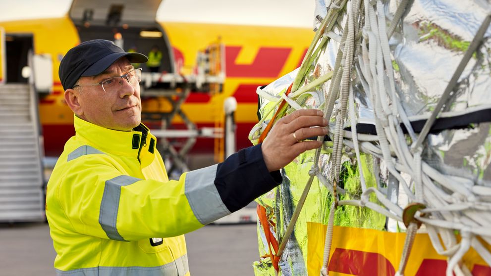 a dhl employee checking the security net of a shipment in front of an aeroplane in which the cargo will be loaded