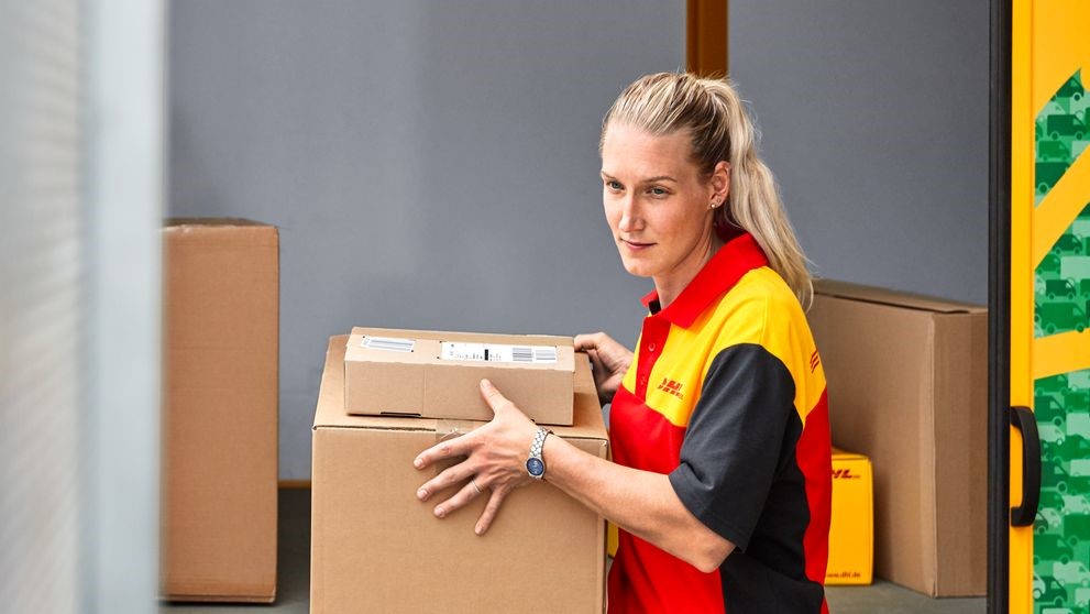 A DHL employee unloads boxes from a DHL GoGreen van.