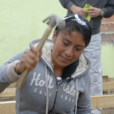 Image_on_a_young_columbian_woman_in_grey_hoodie_swinging_a_hammer_building_a_shelter