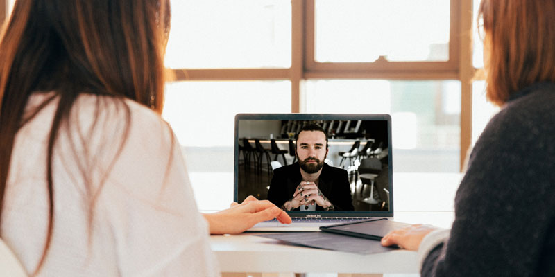 two women speaking to a man on a laptop screen