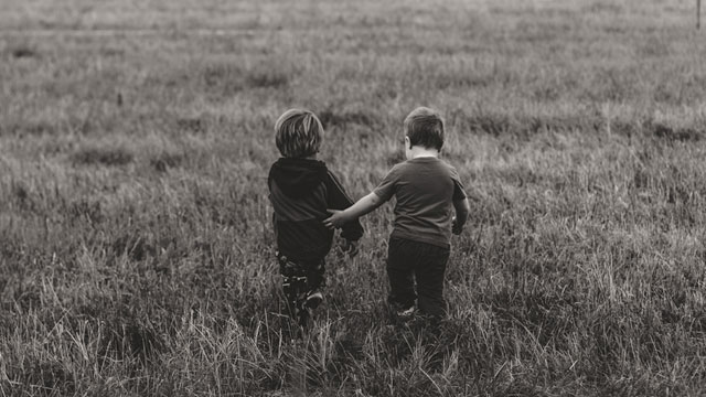 Black and white photo of the backs of two young boys walking in a field