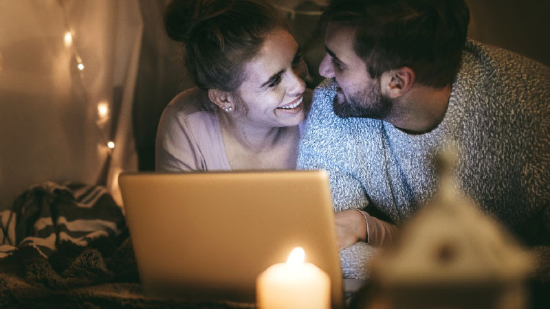 Couple smiling at eachother with laptop and candles