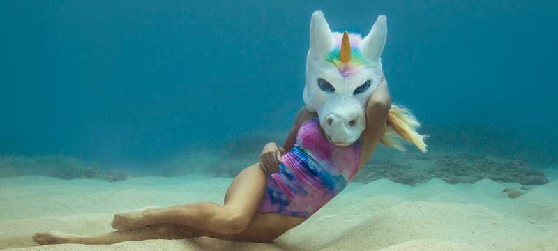 Woman underwater with pink swimsuit and unicorn head on.
