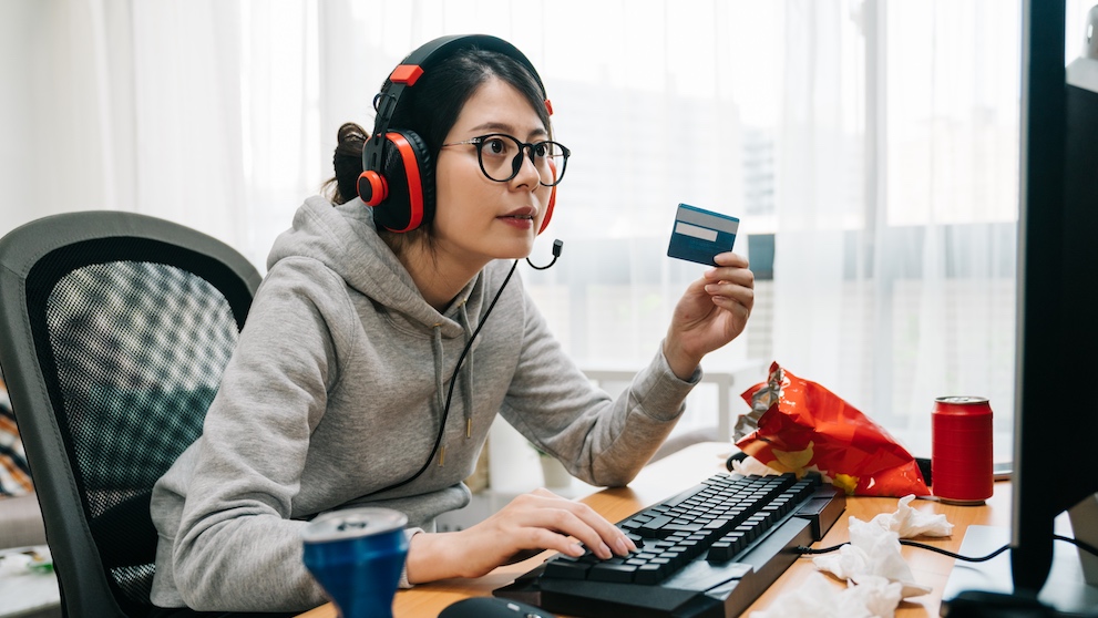 young lazy college girl nerd at home on summer break off from school holding credit card paying online e commerce buying game points. asian woman geek with headphones playing computer internet.