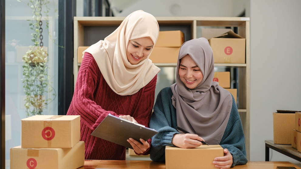 Friend muslim female two work business sme online shopping working on laptop computer with parcel box on desk at home, SME online business and delivery concept