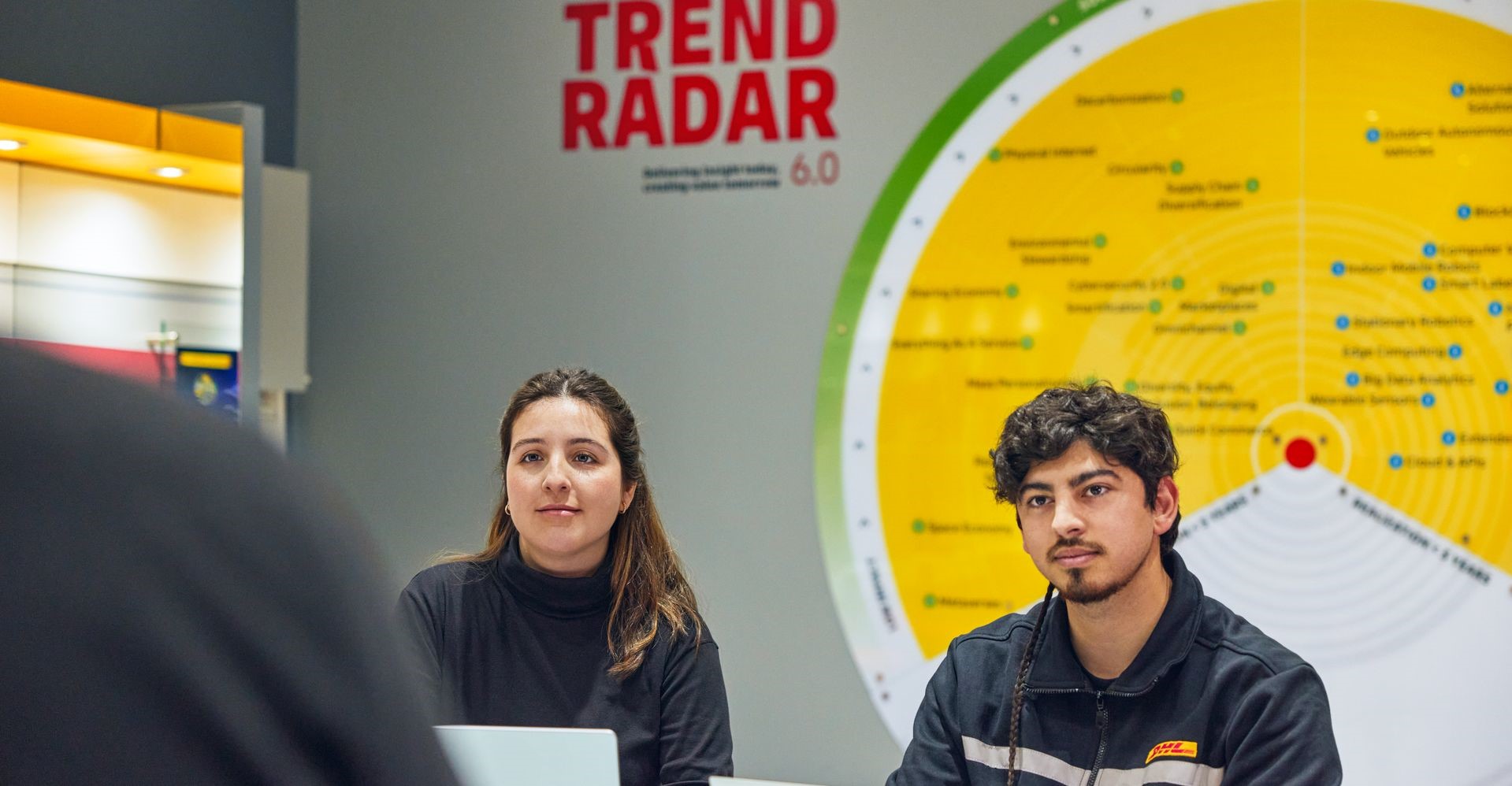 two dhl employees discussing logistics trends in front of a trend radar wall