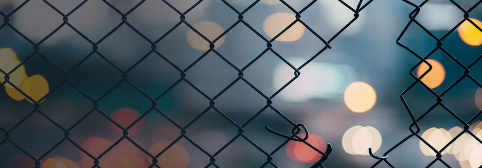 Hole in a metal fence with blurred lights