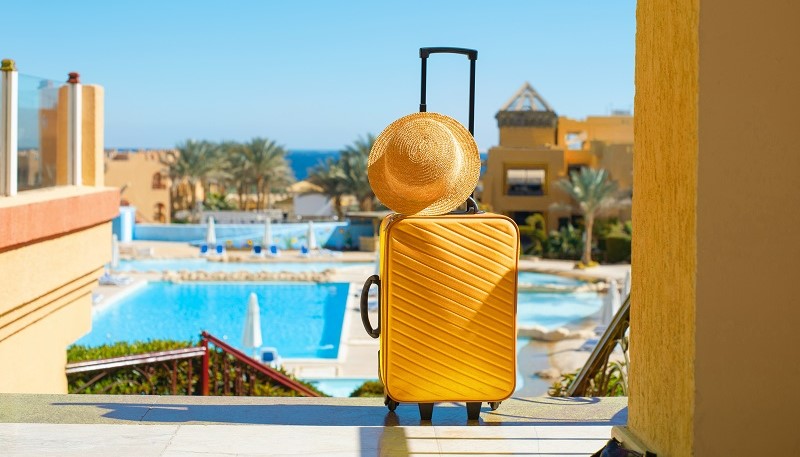 Travel, summer holidays and vacation concept. yellow suitcase with hat on background of hotel pool area in Egypt.